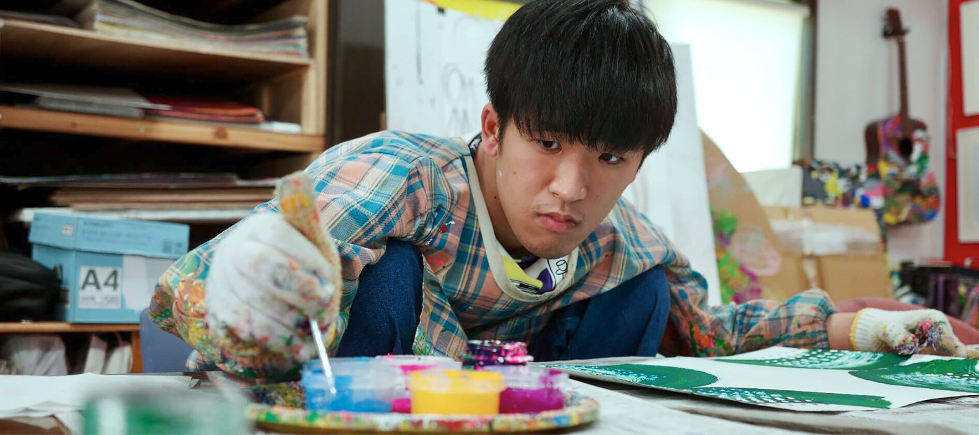 サントリー天然水 SPARKLING Collaboration with Shigaku Mizukami

机に向かい、筆に絵の具をつける水上詩楽（みずかみ・しがく）の斜め横からの姿の写真。下にプロフィール情報が続く。

水上詩楽（みずかみ・しがく）
やまなみ工房、滋賀県

様々な色でいくつも描かれた扇形と点の模様。複数の扇形を小さいほうから順に重ねながら描いていき、その上に溝引き棒で3列の点を打つ。気持ちが穏やかな時ほど、きれいな筆使いで整列された点になる。はたして、イメージしているものがあるのか、それとも動きを楽しんでいるのか。一体全体、何を感じて描いているのかは彼にしか分からない。自室の壁紙は四方八方どこを見ても自身が描いたロゴやアニメキャラクターで埋め尽くされている。